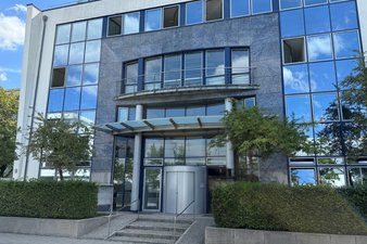 Modernes Bürogebäude, in dessen Fenstern sich blauer Himmel und Wolken spiegeln