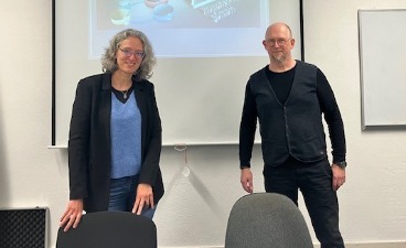 Frau Lebouc von MAut und Herr Mutschler vom idf stehen vor einer Leinwand mit einer Power Point Präsentation